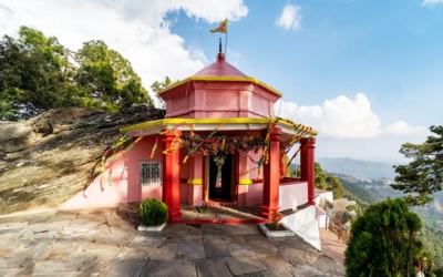 A view from the Kasar Devi Temple complex over the valley, with a small temple structure and surrounding trees